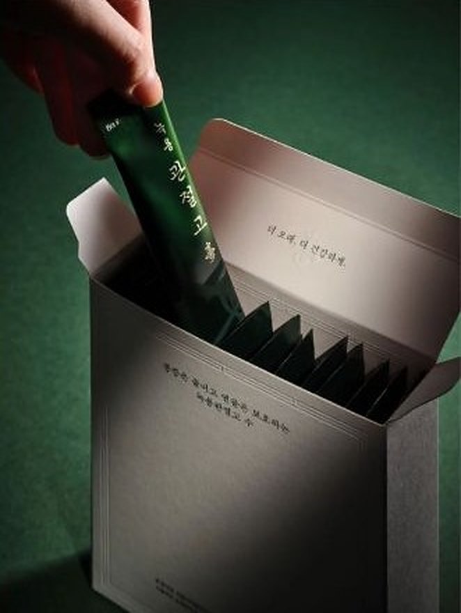 회색 상자에서 초록색 녹용관절고 스틱을 한 포 꺼내는 손